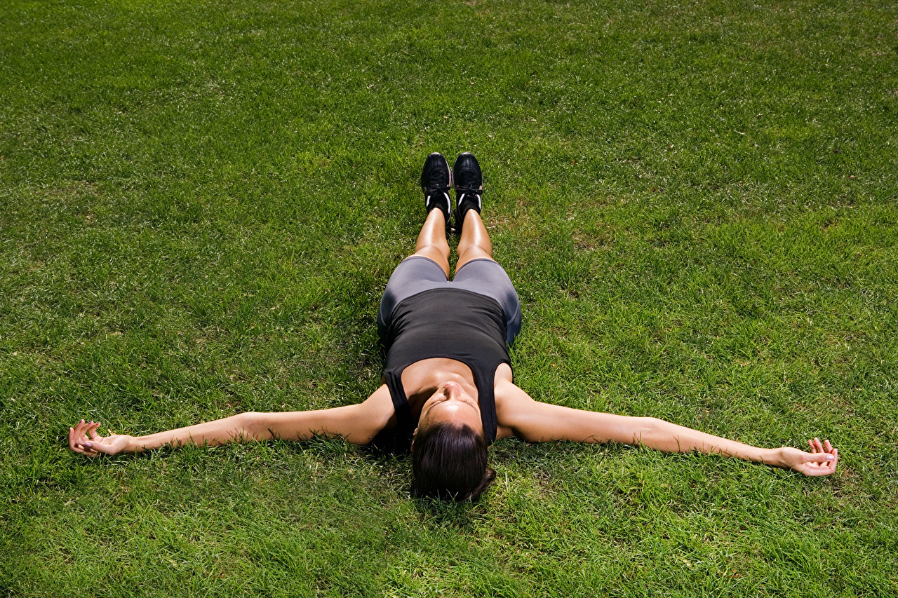 Худая девушка тренируется на гибкость голой лежа на мягком ковре